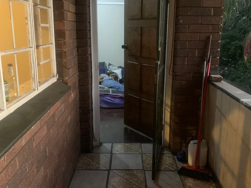 A covered balcony area featuring exposed brick walls and tiled flooring, providing access to the interior through a timber door and security gate.