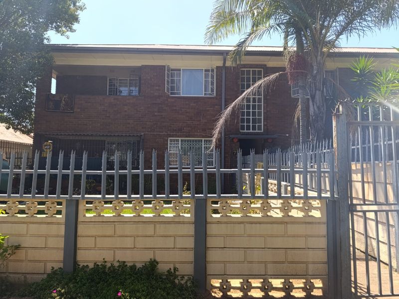 Front elevation of a two-story face brick apartment building featuring secure perimeter fencing, security gates, and window bars.
