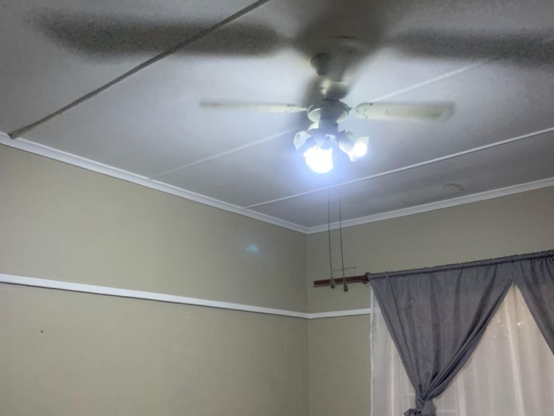 A bedroom featuring a ceiling fan with integrated lighting, picture rails, and visible ceiling staining requiring maintenance.