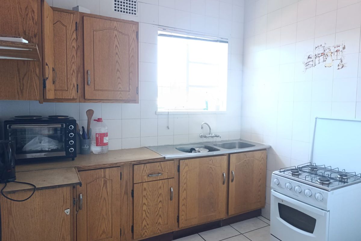 A functional kitchen featuring wooden cabinetry, a double stainless steel sink, tiled splashbacks, and a freestanding gas stove.