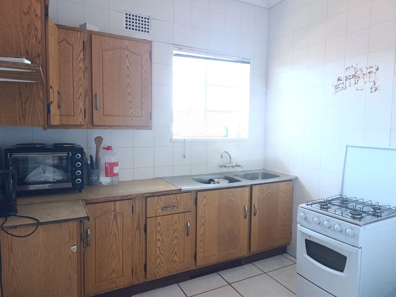 A functional kitchen featuring wooden cabinetry, a double stainless steel sink, tiled splashbacks, and a freestanding gas stove.