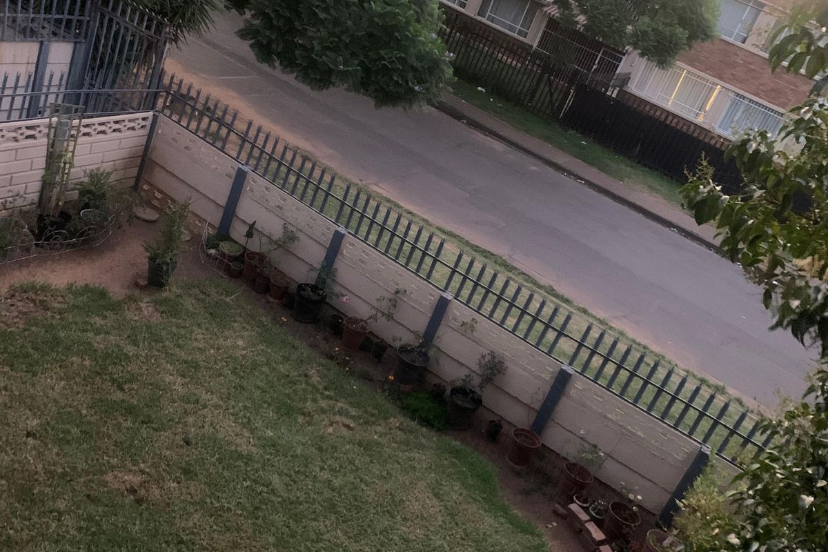 A view of the property's garden area featuring a lawn, perimeter wall, and metal security fencing.