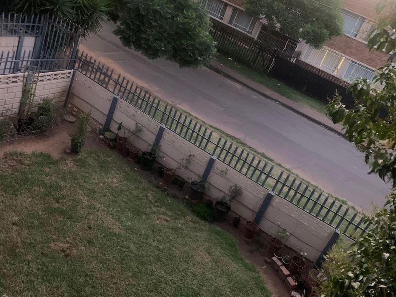A view of the property's garden area featuring a lawn, perimeter wall, and metal security fencing.