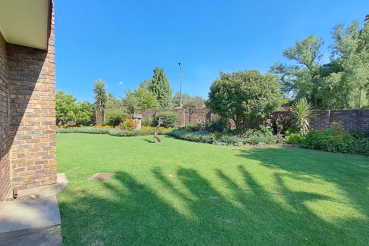 A well-maintained rear garden featuring a lush green lawn, established garden beds, and a solid brick boundary wall.