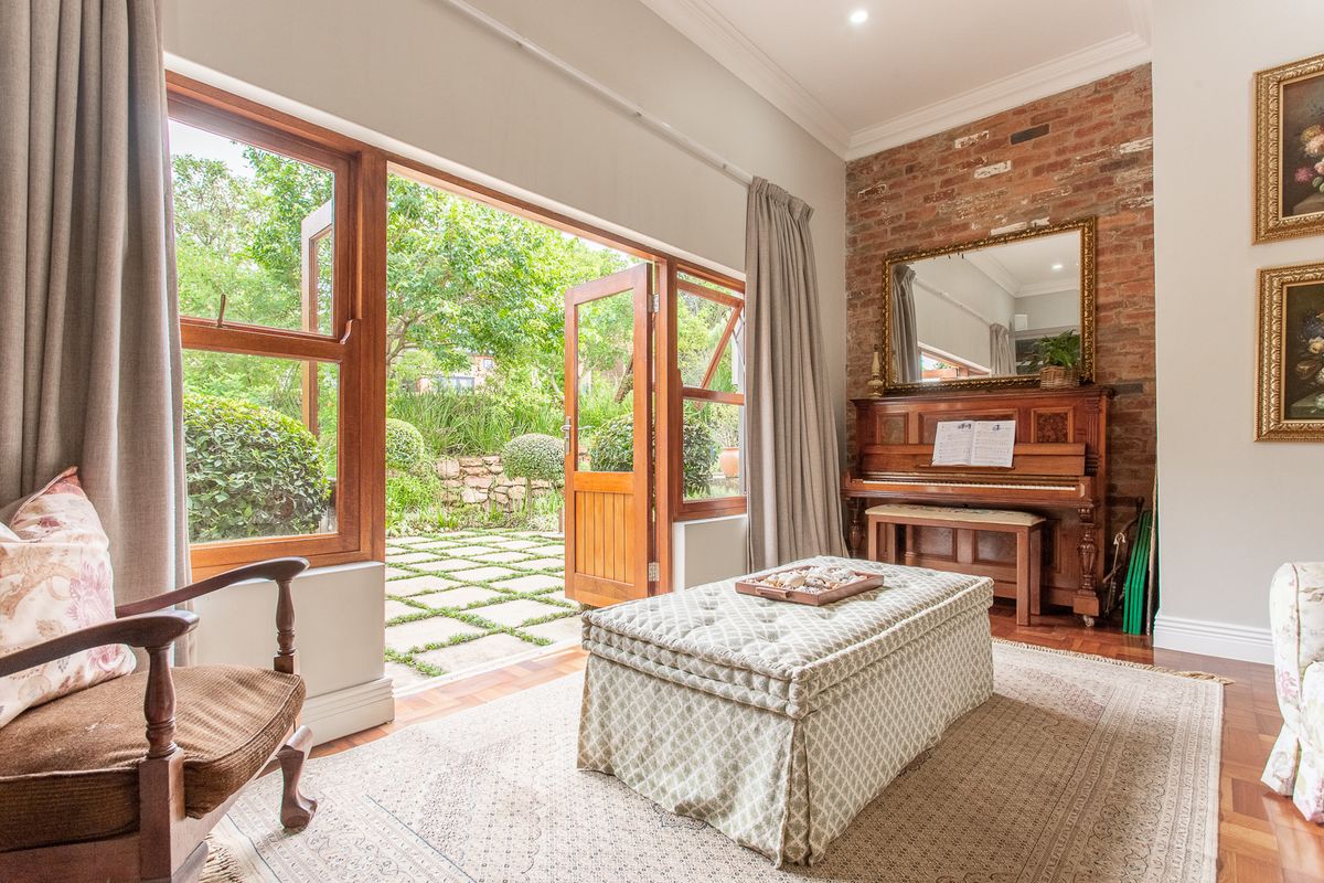 A bright living room featuring parquet flooring, an exposed brick feature wall, and large timber-framed doors opening onto a landscaped garden patio.