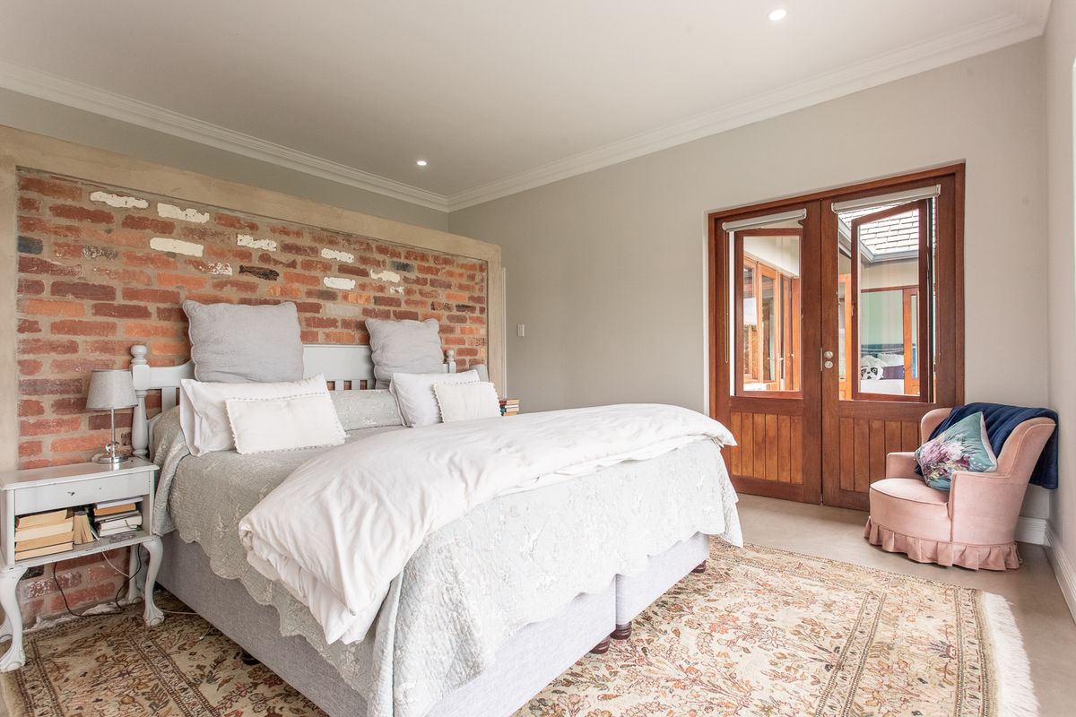 Spacious bedroom featuring an exposed brick feature wall, neutral finishes, and timber-framed double doors providing access to an outdoor area.