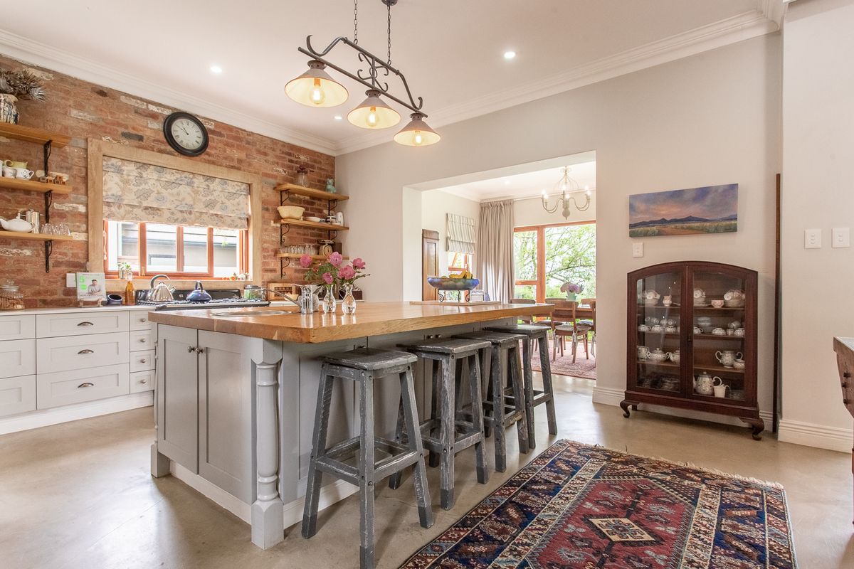A well-appointed kitchen featuring an island with a wooden countertop, exposed brick wall, and open shelving, seamlessly flowing into the adjacent dining area.