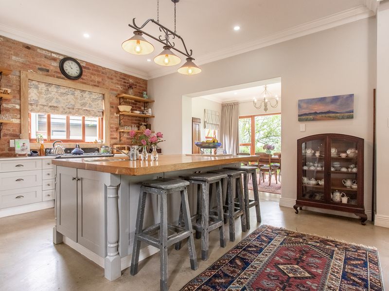A well-appointed kitchen featuring an island with a wooden countertop, exposed brick wall, and open shelving, seamlessly flowing into the adjacent dining area.