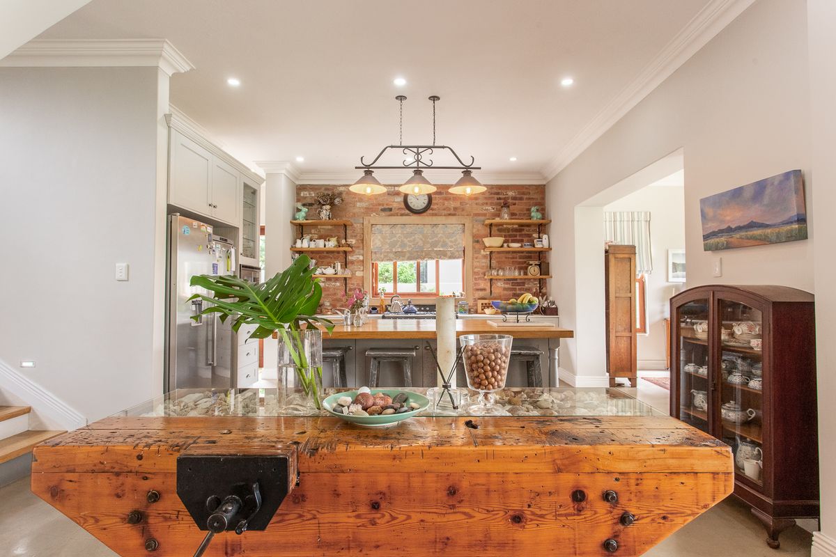 A charming kitchen featuring an exposed brick wall, timber shelving, and a central island, creating a warm and inviting culinary space.