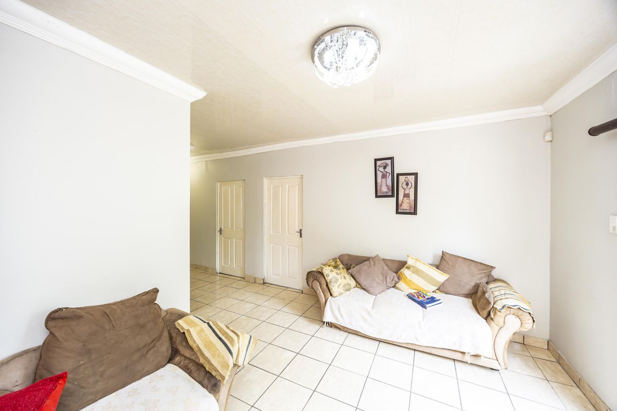 A bright living room featuring neutral tiled flooring, coved ceilings, and access to internal hallways and rooms.