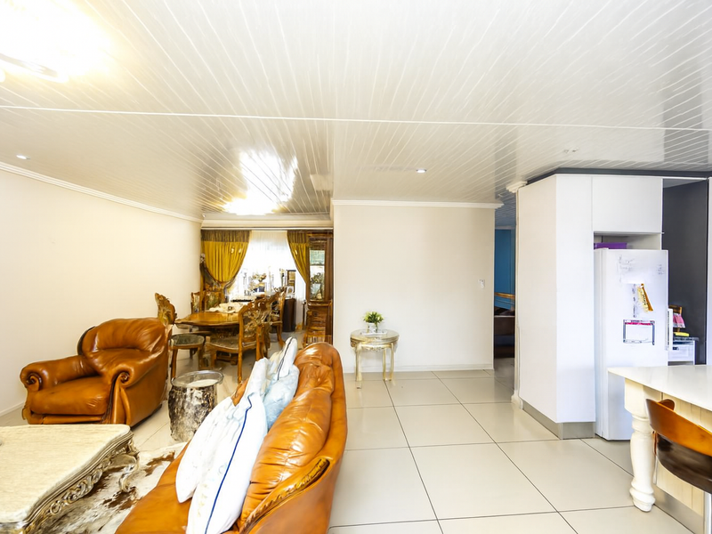 An open-plan living and dining area featuring large format floor tiles and a glossy panelled ceiling, seamlessly connected to a functional kitchen space.
