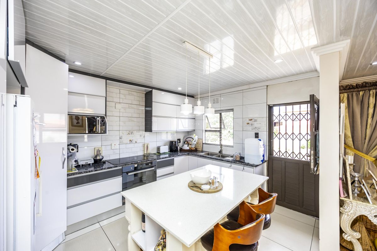Modern kitchen featuring high-gloss cabinetry, stone countertops, a central island, built-in appliances, and direct access to the exterior via a security gate.