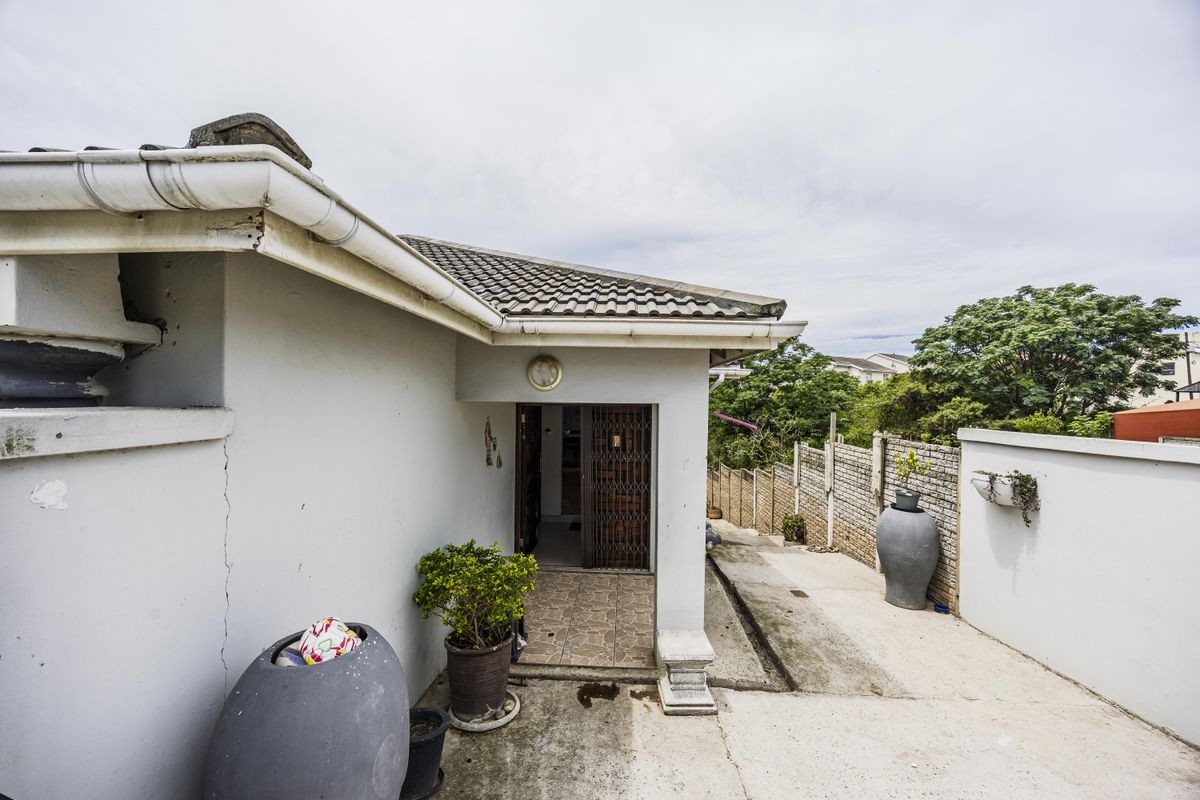 Rear exterior view of the property featuring a concrete driveway, tiled roof, and secure entrance gate with surrounding brick boundary walls.