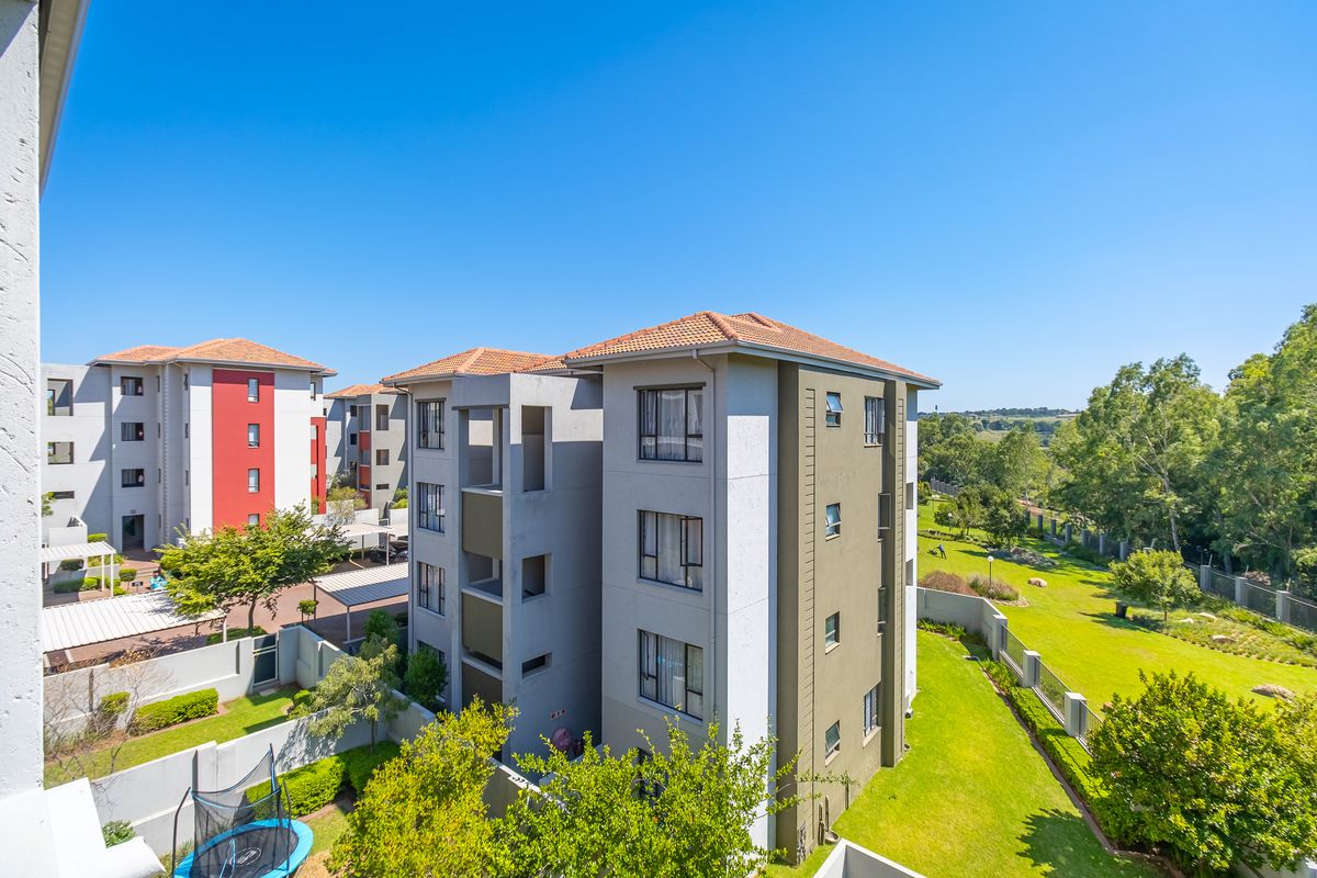 An elevated aerial view of a modern apartment complex featuring multi-story buildings with terracotta roofs, landscaped grounds, and surrounding perimeter walls.
