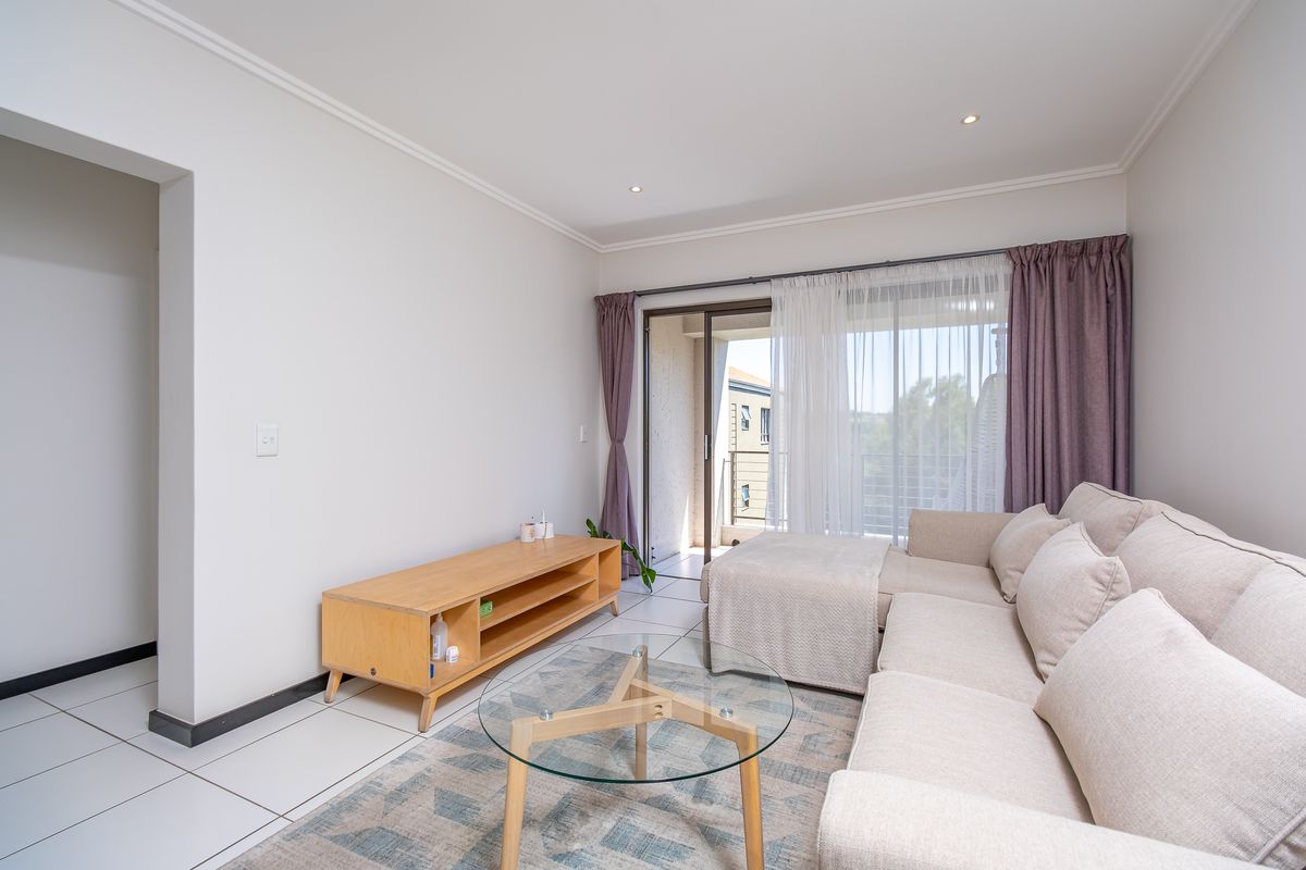 A bright and well-maintained living room featuring tiled floors, recessed lighting, and a sliding glass door providing access to a private balcony.