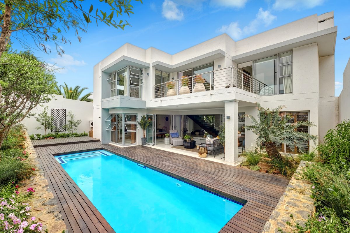 Modern double-story residence featuring a swimming pool, timber decking, and a spacious upper-level balcony overlooking the rear garden area.