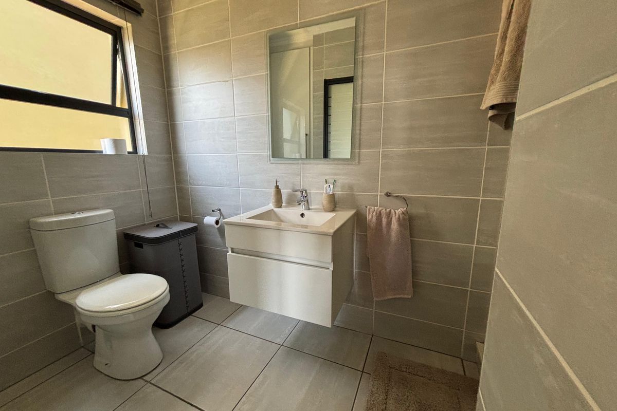 Modern bathroom featuring a wall-mounted vanity, ceramic basin, toilet, and neutral floor-to-ceiling tiling with a top-hung window for natural light.