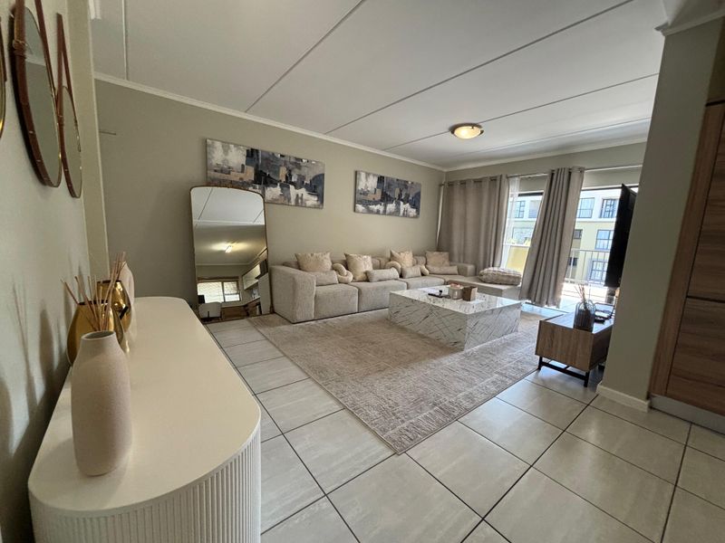 Spacious living room featuring neutral tiled flooring, modern ceiling lighting, and a large sliding glass door providing access to the balcony.