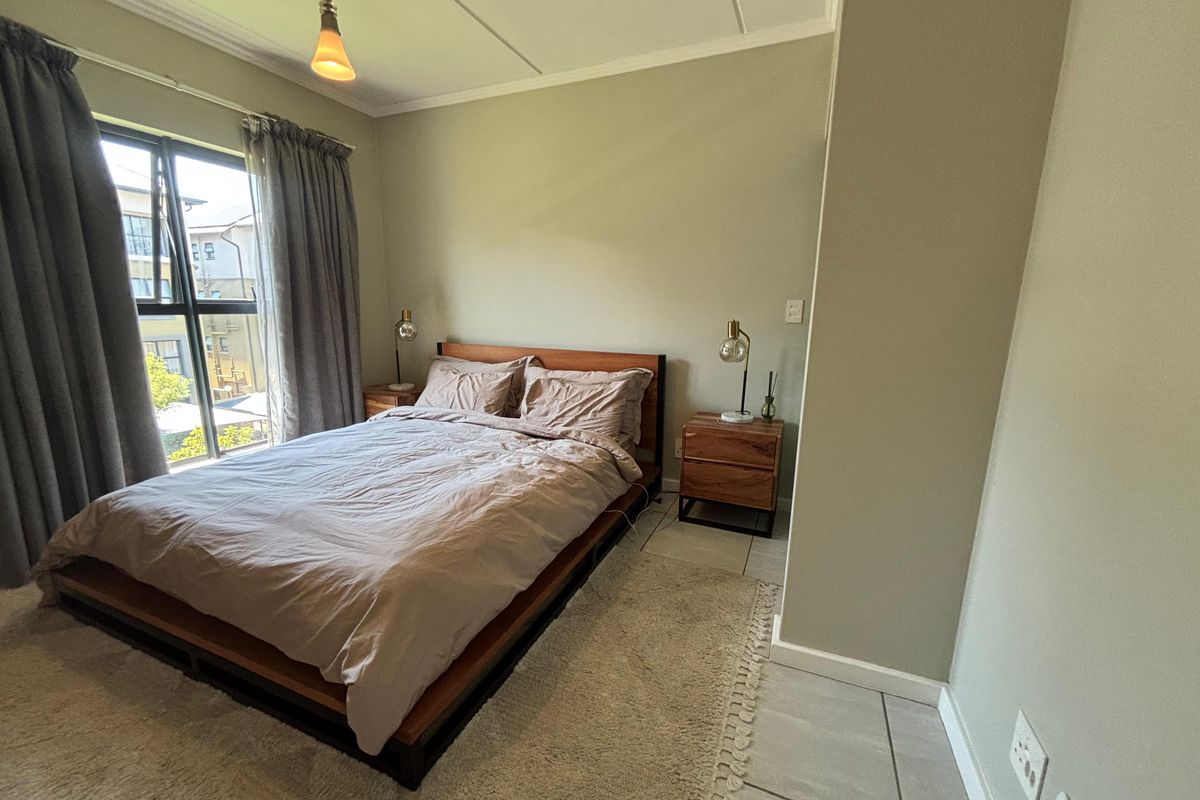 A well-lit bedroom featuring neutral wall tones, tiled flooring, and a large window providing natural light.