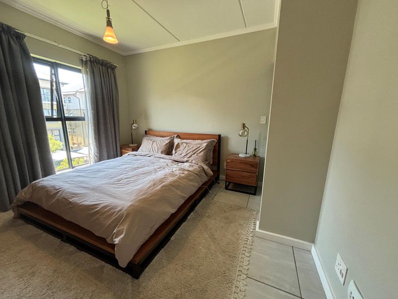 A well-lit bedroom featuring neutral wall tones, tiled flooring, and a large window providing natural light.
