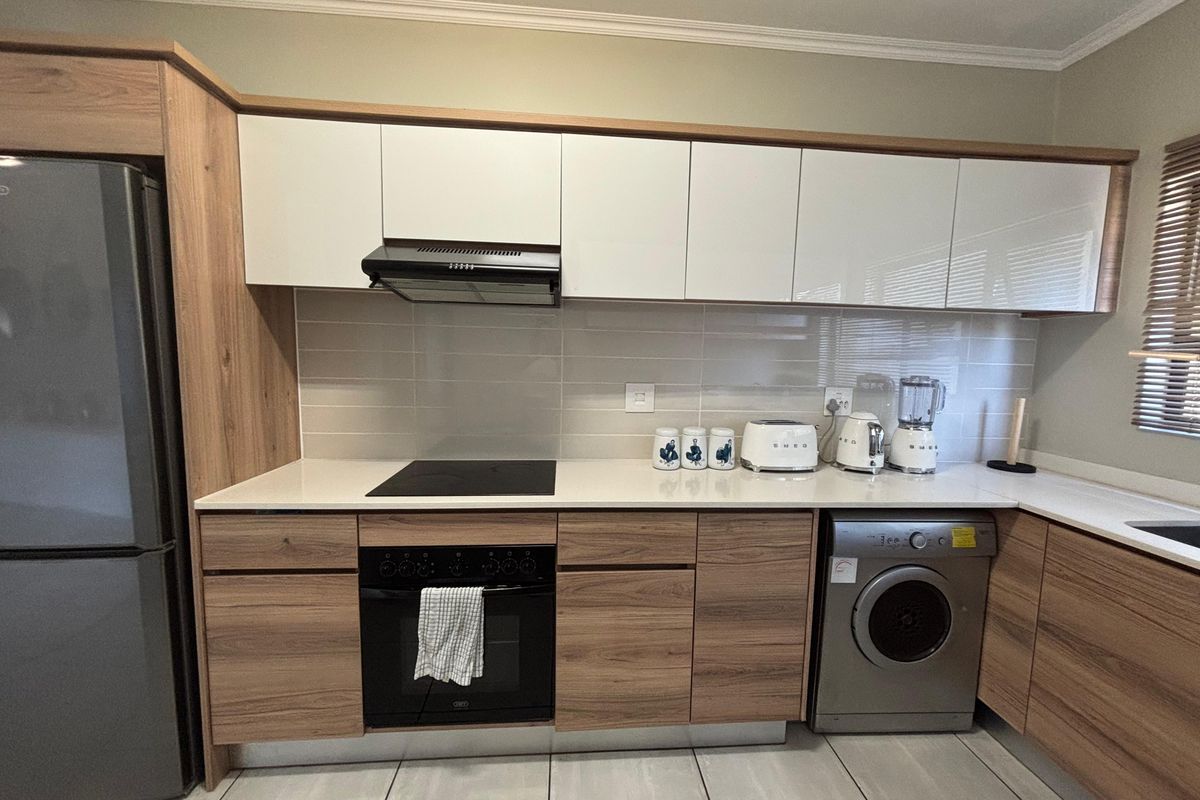 Modern kitchen featuring wood-grain cabinetry, white upper cabinets, quartz countertops, integrated oven, electric hob, and a tiled backsplash.