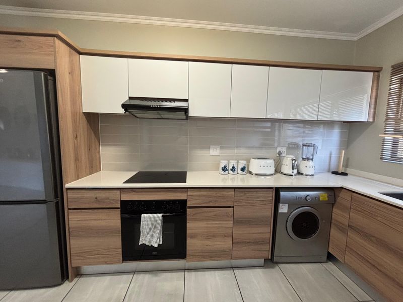 Modern kitchen featuring wood-grain cabinetry, white upper cabinets, quartz countertops, integrated oven, electric hob, and a tiled backsplash.