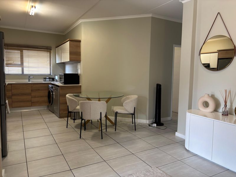An open-plan kitchen and dining area featuring modern wood-finish cabinetry, tiled flooring, and integrated laundry appliances, creating a functional and cohesive living space.