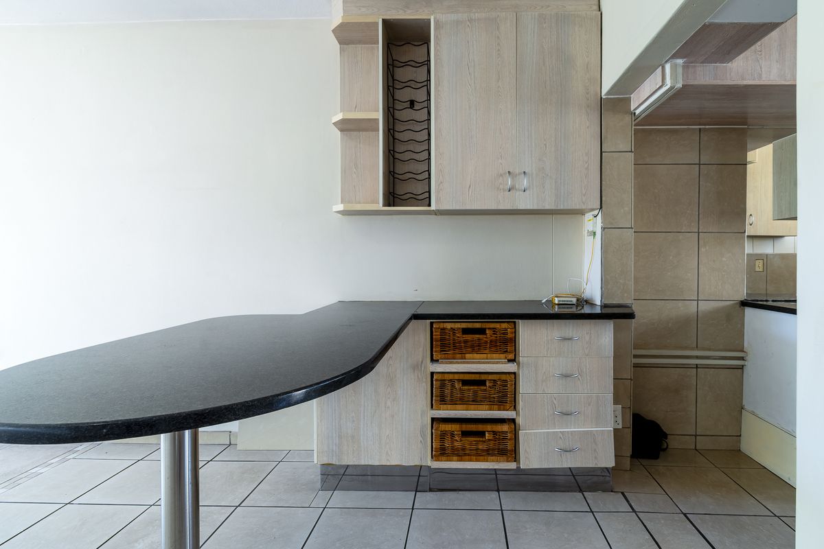 A functional kitchen area featuring light wood-grain cabinetry, a black stone breakfast bar, and neutral ceramic floor and wall tiling.