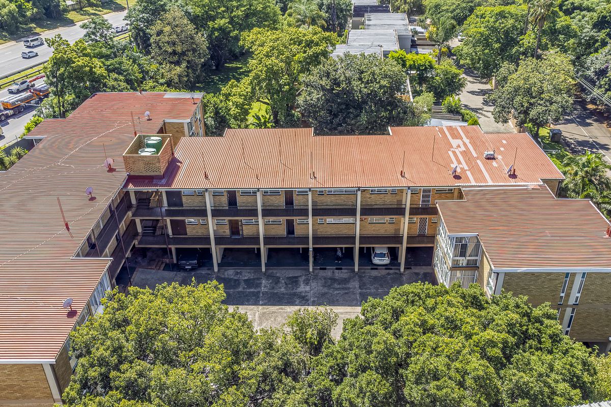 Aerial view of a multi-story apartment complex featuring a corrugated metal roof, brick exterior, and ground-level covered parking area.