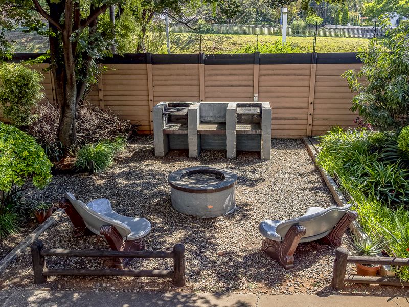 A landscaped garden area featuring a built-in concrete braai, a central fire pit, and a perimeter precast wall.