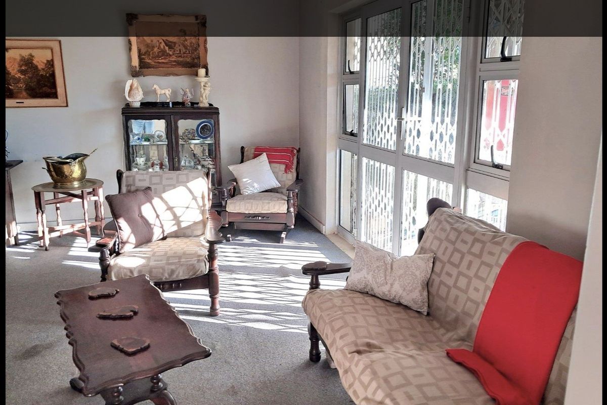 A living room featuring carpeted flooring and large aluminium sliding doors with integrated security gates, providing natural light and access to the exterior.