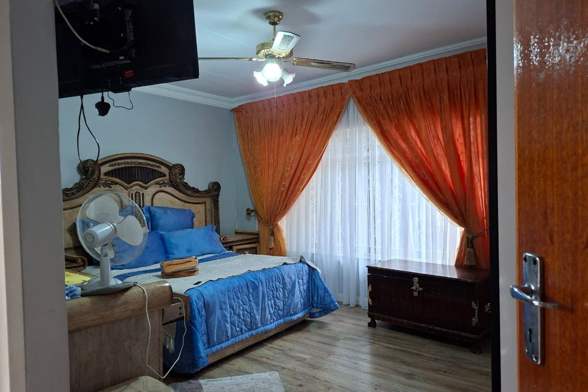 A bedroom featuring wood-look flooring, a ceiling fan, and large windows with curtains.