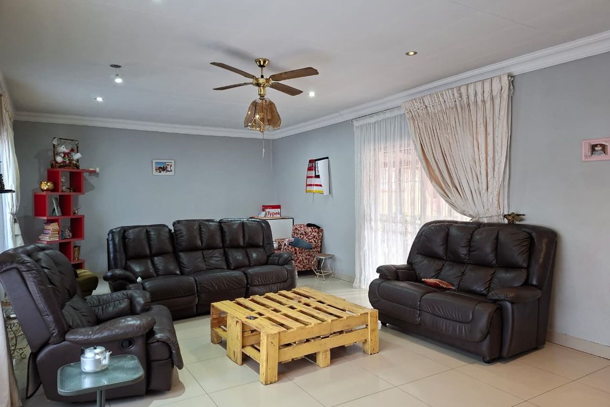 A spacious living room featuring tiled flooring, recessed downlighting, and a ceiling fan, with large windows dressed in curtains.
