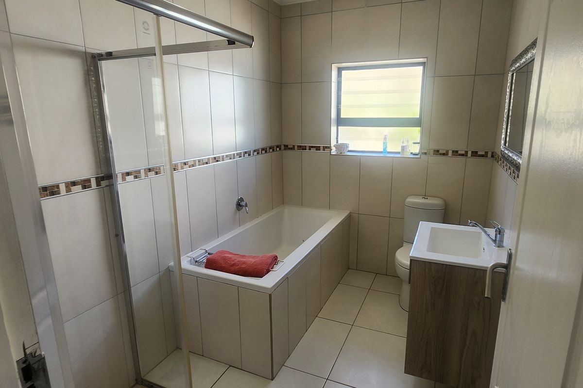 A modern bathroom featuring a built-in bathtub, a separate glass-enclosed shower, a vanity basin, and a toilet with neutral wall and floor tiling.