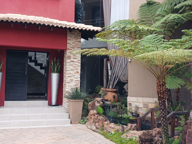 Front entrance featuring a covered porch with stone cladding, tiled roof, and a landscaped garden area with a water feature.