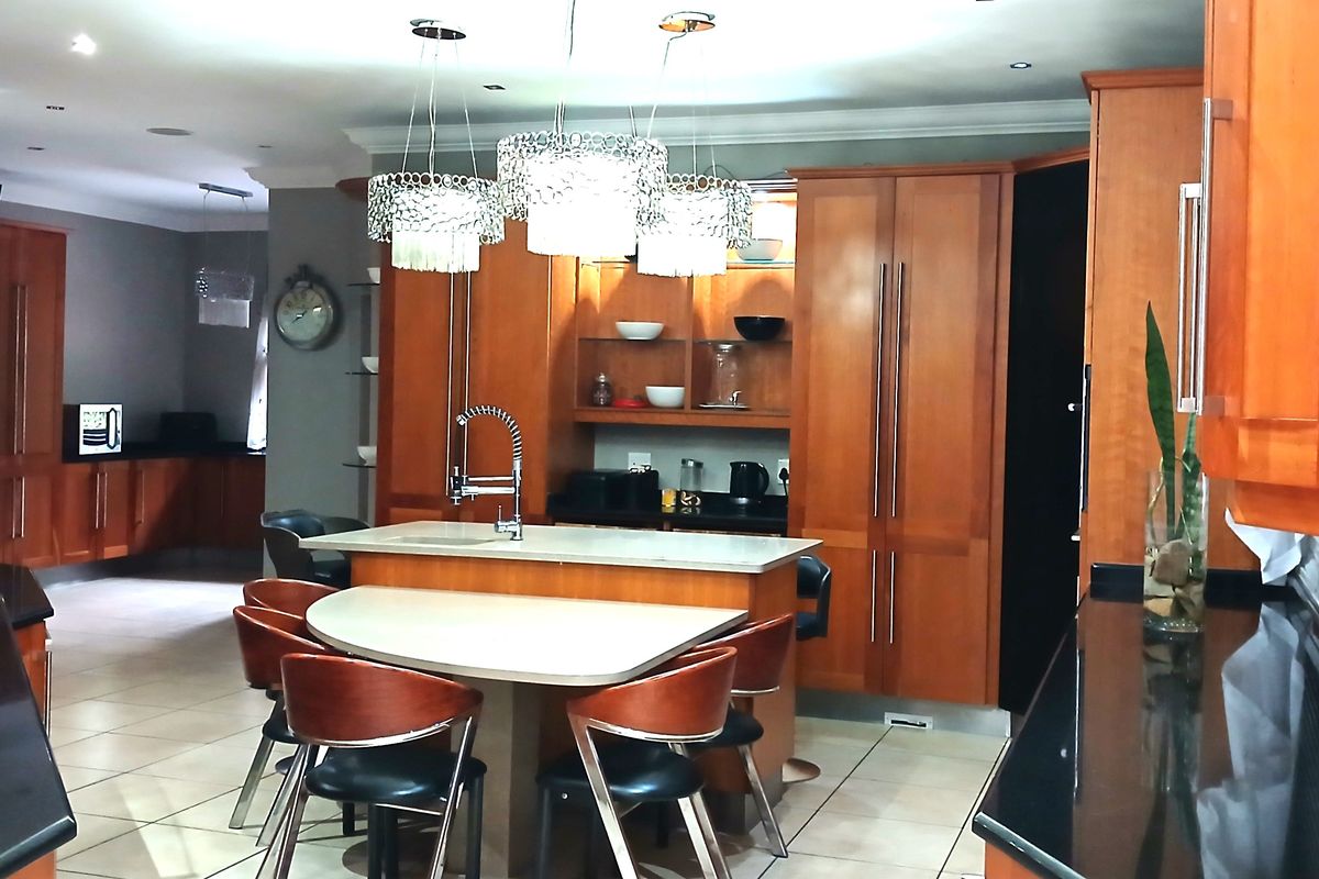 Spacious kitchen featuring warm-toned wooden cabinetry, a central island with integrated seating, stone countertops, and modern pendant lighting.