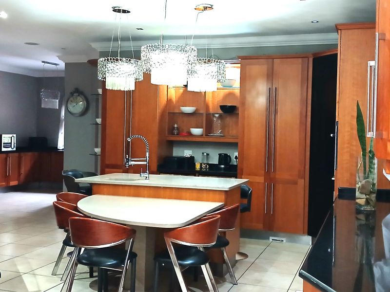 Spacious kitchen featuring warm-toned wooden cabinetry, a central island with integrated seating, stone countertops, and modern pendant lighting.