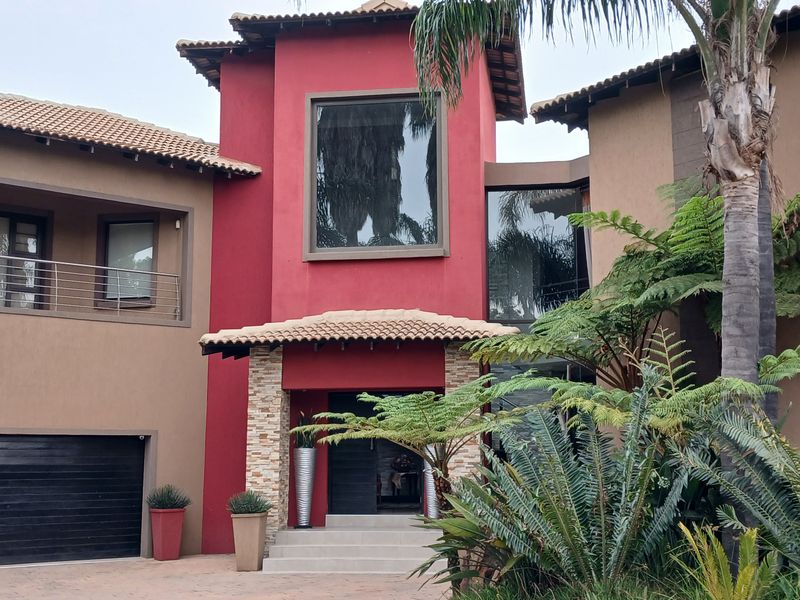 A striking double-story residential facade featuring a bold red central tower, stone cladding accents, a balcony, and an integrated double garage.