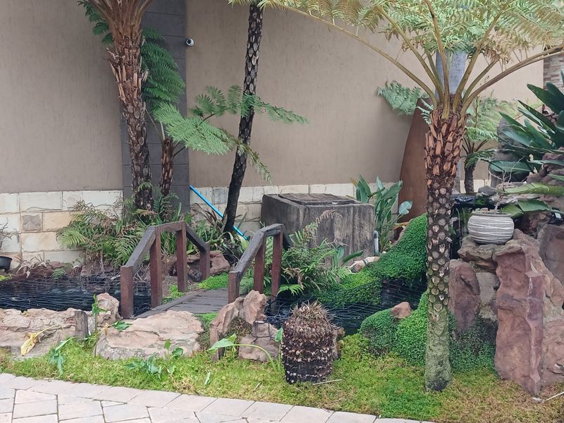 A landscaped garden area featuring a stone-lined water feature, a small wooden bridge, and decorative stone elements adjacent to the building exterior.