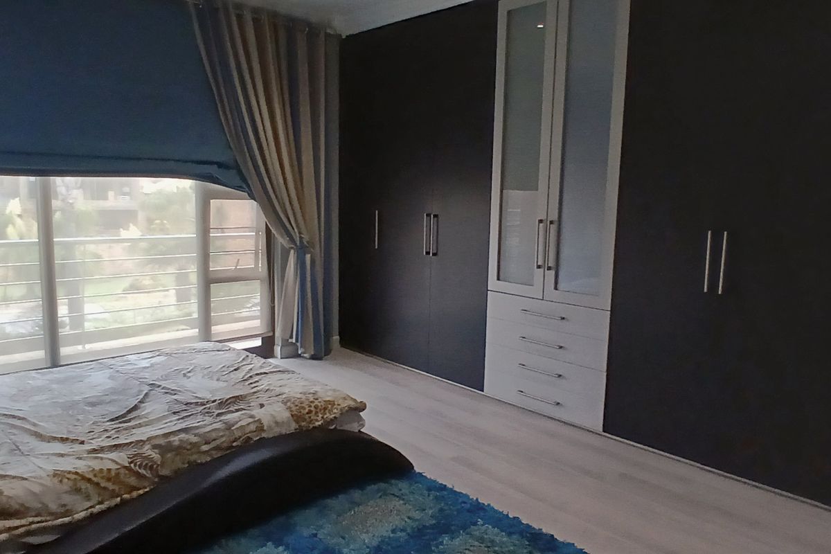 A bedroom featuring extensive dark built-in cupboards, light laminate flooring, and a large sliding glass door providing natural light and outdoor access.
