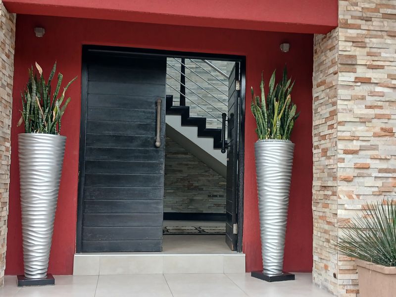 Modern entrance featuring a striking red facade with stone veneer accents and a large, contemporary pivot door leading into the home.