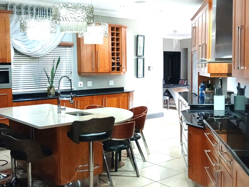 Spacious kitchen featuring warm wood cabinetry, a central island with integrated sink, stone countertops, and built-in appliances, offering a functional and well-appointed cooking space.