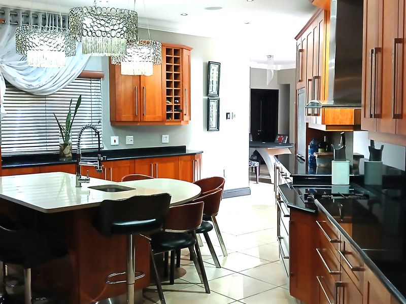 Spacious kitchen featuring warm wood cabinetry, black stone countertops, a central island with seating, and integrated appliances.