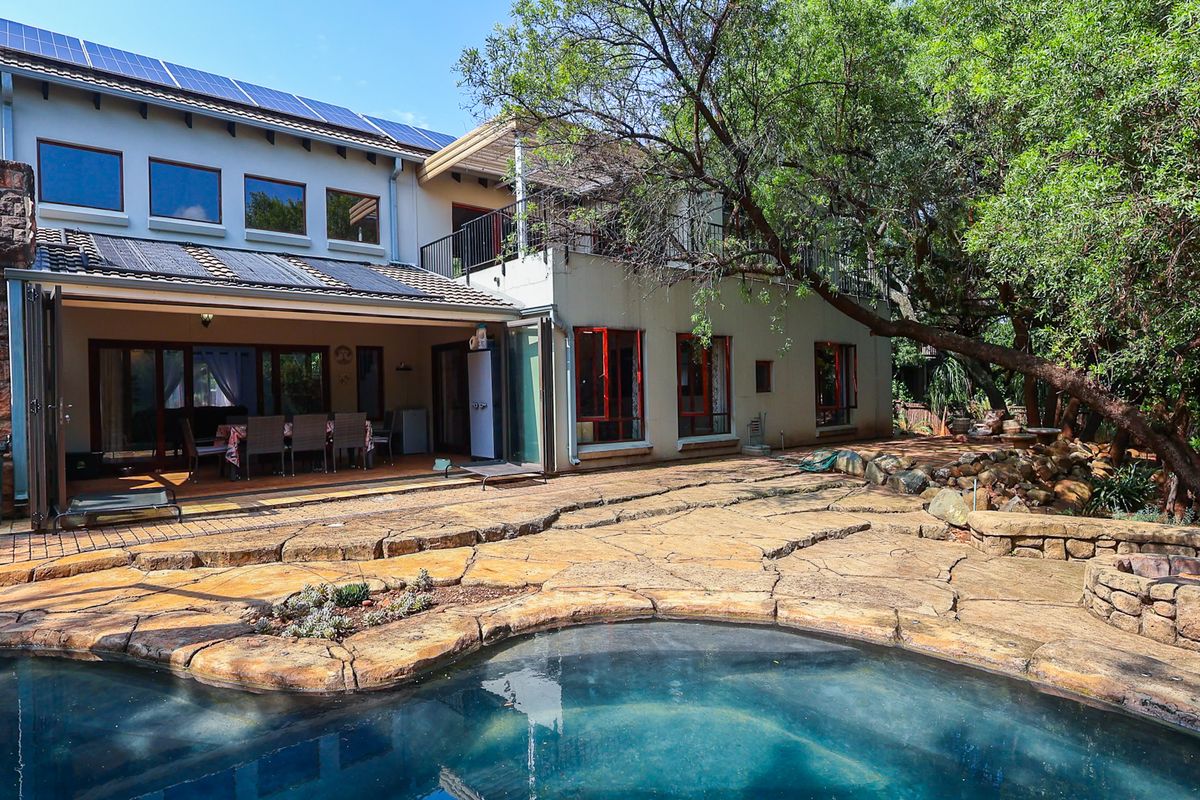 Rear exterior view featuring a swimming pool, stone-paved patio area, built-in fire pit, and a multi-level home with solar panels and balcony access.
