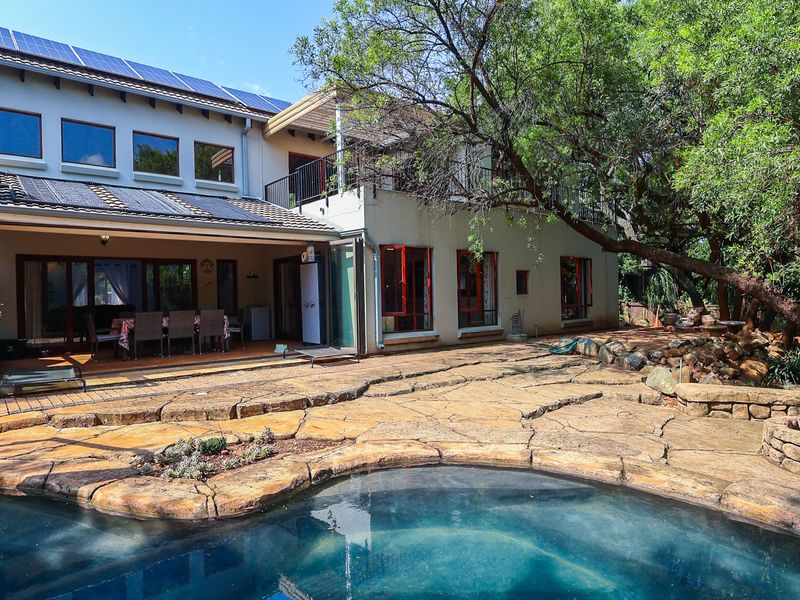 Rear exterior view featuring a swimming pool, stone-paved patio area, built-in fire pit, and a multi-level home with solar panels and balcony access.