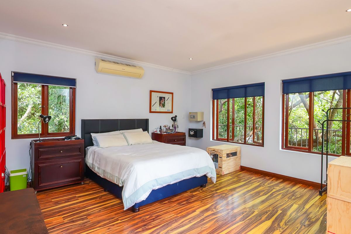 Spacious bedroom featuring polished timber flooring, recessed lighting, air conditioning, and large windows with views of the surrounding greenery.