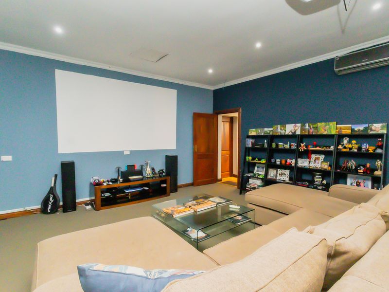 A dedicated cinema room featuring a large projector screen, recessed downlighting, and a wall-mounted split-system air conditioning unit.