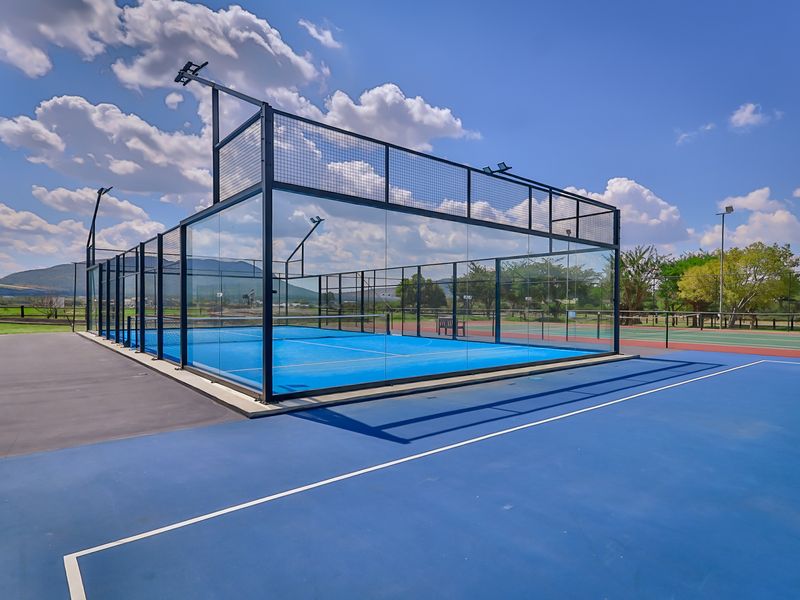 A well-maintained outdoor sports facility featuring a modern padel court with glass perimeter fencing and adjacent tennis court infrastructure.