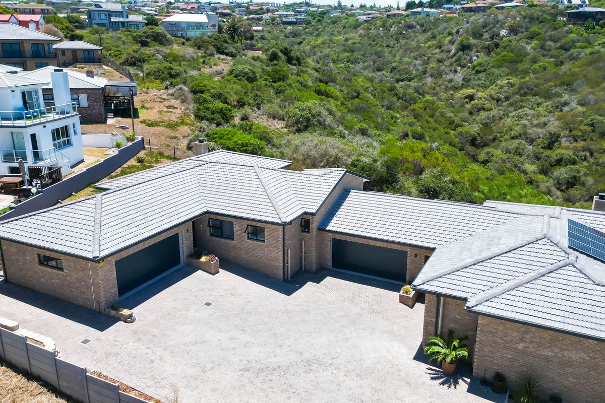 Aerial view of a modern brick house featuring a spacious paved driveway, double garages, and solar panels installed on the tiled roof.
