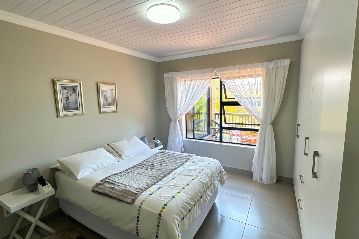 A well-maintained bedroom featuring tiled flooring, built-in wardrobes, and a large window providing natural light and access to an outdoor balcony area.